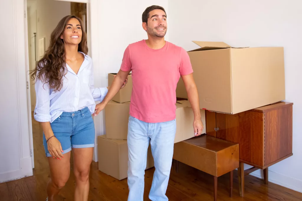 happy excited young couple looking their new apartment with carton boxes furniture smiling at Melbourne